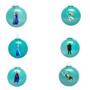 May include: Six turquoise blue Christmas ornaments with various Frozen characters and images. The ornaments feature Elsa, Anna, Olaf, Kristoff, Sven the reindeer, and a scene of Elsa and Anna together.