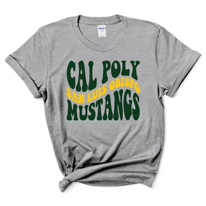 May include: A heather gray t-shirt with the words "CAL POLY SAN LUIS OBISPO MUSTANGS" in a retro font. The text is in green and yellow. The shirt has rolled-up sleeves and a crew neck.