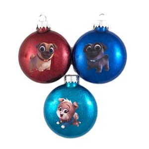 May include: Three Christmas ornaments featuring different cartoon pugs. The ornaments are round and have a glitter finish. One ornament is red, one is blue, and one is teal.