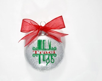 May include: Silver glitter Christmas ornament with a red bow. The ornament has a green design of hairdressing tools and the name "Traci" in red.