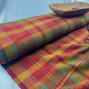 May include: A roll of plaid fabric in shades of red, orange, green, and brown. The fabric has a soft, fuzzy texture.