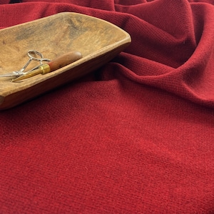 Puede incluir: Un cuenco de madera sobre un fondo de tela roja. El cuenco está vacío y tiene un acabado de madera natural. Hay dos pequeñas herramientas dentro del cuenco, una con un mango de madera y otra con un mango de metal.