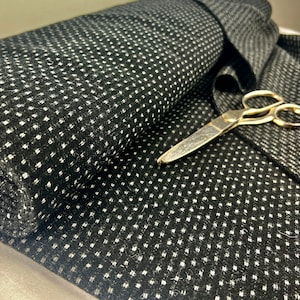May include: Black fabric with a white polka dot pattern. The fabric is folded and a pair of gold scissors are lying on top of it.