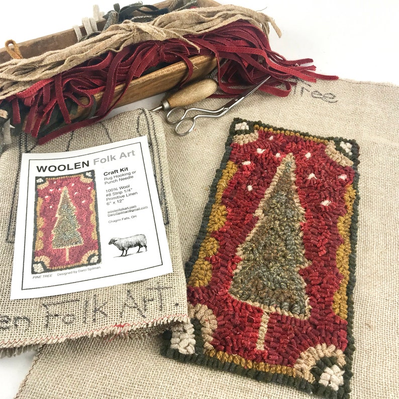 May include: A craft kit for rug hooking or punch needle, featuring a completed rug with a Christmas tree design. The kit includes wool strips, a needle, and a linen base. The finished rug measures 6 x 12 inches.