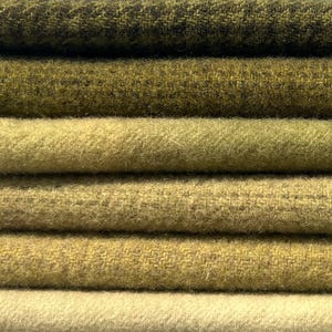 May include: A stack of six folded fabric pieces in varying shades of green and yellow. The textures range from a dark olive houndstooth pattern at the top to a smooth, light cream-colored felted textile at the bottom, showing distinct weaves.
