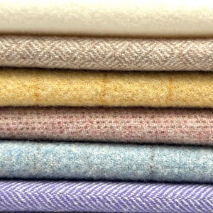 May include: Close-up of a stack of colorful fabric samples. The fabrics include cream, tan herringbone, yellow, pink, light blue, and purple herringbone patterns. The textures appear soft and woven, suitable for textiles.