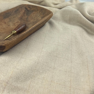 May include: A rustic wooden bowl with a dark brown finish, holding a leather and brass awl. The bowl sits on a beige, textured fabric, creating a neutral and earthy aesthetic.