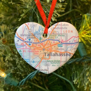 May include: A heart-shaped ornament with a map of Tallahassee, Florida. The ornament is red and white and features the text "Tallahassee" and "Leon" on the map.