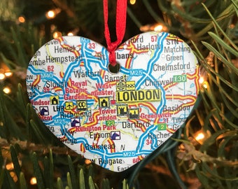 May include: A heart-shaped Christmas ornament with a map of London, England. The ornament is white with blue, red, and green details. The map includes landmarks like the Tower of London, Buckingham Palace, and the Houses of Parliament.