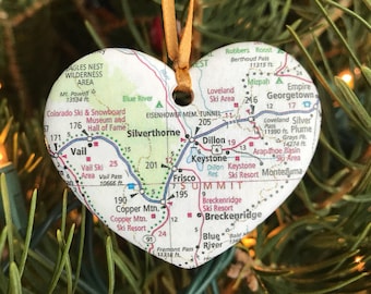 Puede incluir: Un adorno navideño en forma de corazón con un mapa de las estaciones de esquí de Colorado. El adorno está decorado con los nombres de las estaciones, incluyendo Vail, Breckenridge, Keystone y Copper Mountain. El adorno está colgado de un árbol de Navidad.