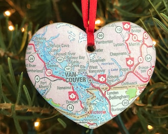 May include: A heart-shaped Christmas ornament featuring a vintage map of Vancouver Island, British Columbia. The ornament is red and white with the text "VANCOUVER" in bold red letters.