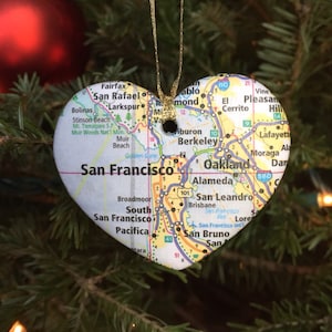 May include: A heart-shaped Christmas ornament made from a map of the San Francisco Bay Area. The ornament is hanging on a green Christmas tree.