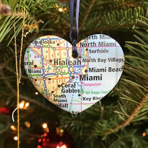 May include: A heart-shaped Christmas ornament featuring a map of Miami, Florida. The ornament is made of paper and has a black ribbon for hanging. The map shows various neighborhoods and landmarks, including Opa-locka, Hialeah, Coral Gables, North Miami, Surfside, North Bay Village, Miami Beach, and Miami.
