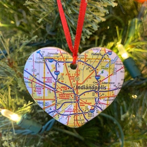 May include: A heart-shaped Christmas ornament featuring a map of Indianapolis, Indiana. The ornament is red and white with black text and numbers. The map shows major roads and highways, including Interstate 65, Interstate 70, and Interstate 465.