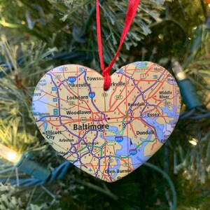 May include: A heart-shaped ornament with a map of Baltimore, Maryland. The ornament is decorated with highway numbers and city names, including Towson, Pikesville, Lochearn, Woodlawn, Baltimore, Dundalk, Rosedale, Essex, and Middle River.