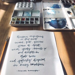 May include: A handwritten quote on a white piece of paper with a blue ink pen. The quote reads: "Christian contentment is that sweet inward, quiet, gracious frame of spirit, which freely submits to and delights in God's wise and fatherly disposal in every condition." The quote is attributed to Jeremiah Burroughs.