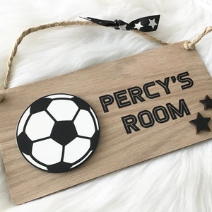 May include: Wooden sign featuring a football graphic and the text "PERCY'S ROOM". The sign is designed with a rope for hanging, two black star accents, and a black and white star ribbon.