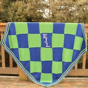May include: A green and blue checkered knitted blanket with a white border and the initials "EJL" embroidered in the centre.