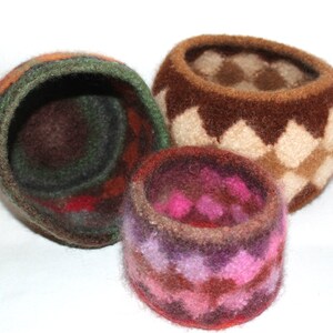 May include: Three felted wool baskets in different sizes and patterns. The largest basket is brown with a diamond pattern, the medium basket is brown, green, and red with a swirling pattern, and the smallest basket is brown, pink, and purple with a swirling pattern.