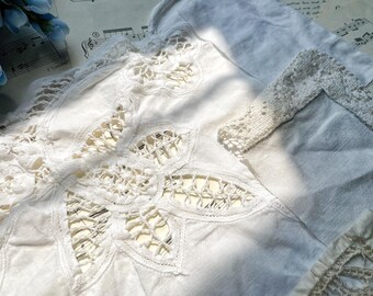 Puede incluir: Primer plano de textiles de lino blanco con intrincados detalles de encaje. El diseño presenta un gran motivo floral con patrones recortados y bordes delicados. También se ven piezas adicionales con adornos de encaje.