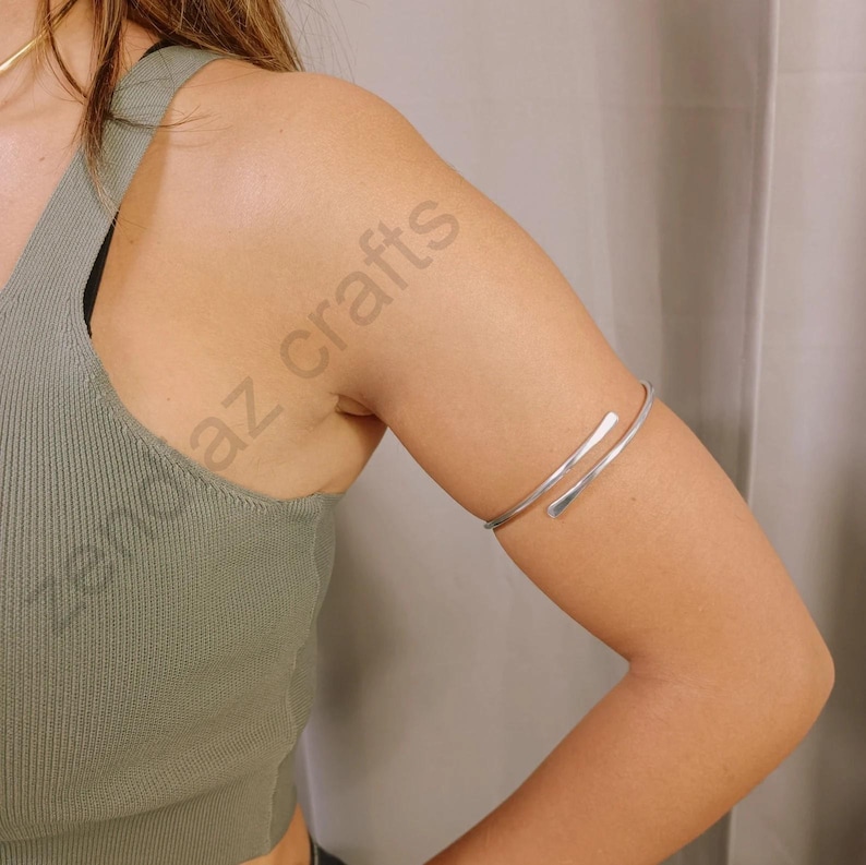 May include: A silver arm cuff bracelet with a simple design. The bracelet is open and adjustable to fit different arm sizes.