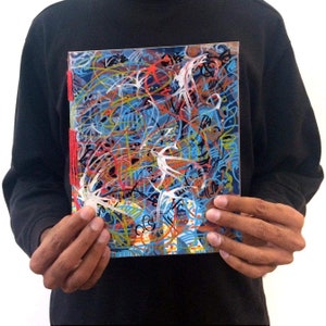 Pode incluir: Uma pintura abstrata colorida com um esquema de cores azul, vermelho, amarelo, branco e preto. A pintura está em tela e tem uma superfície texturizada. A pintura é emoldurada em uma moldura de plástico transparente.