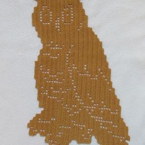 Peut inclure: Napperon en crochet en forme de hibou de couleur moutarde. La forme du hibou est créée avec une série de points et d'espaces ouverts, lui donnant un aspect délicat et ajouré. Le napperon est posé sur une surface blanche et texturée. Les yeux et les détails du corps du hibou sont visibles.