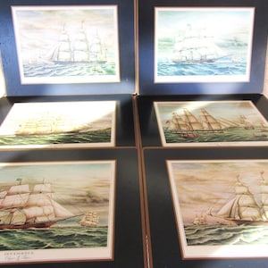May include: A set of six rectangular placemats featuring nautical illustrations of sailing ships on the ocean. Each placemat has a dark blue border and a white inner frame surrounding the detailed maritime artwork of various tall ships at sea.