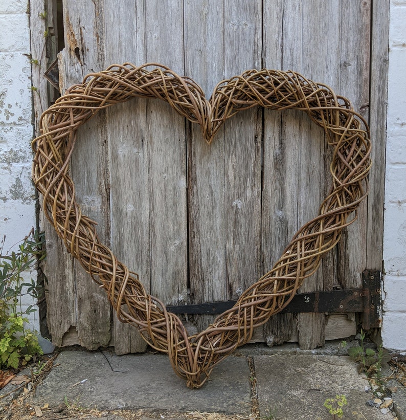 Op de afbeelding: Een grote hartvormige krans gemaakt van gevlochten twijgen, hangend aan een houten deur.
