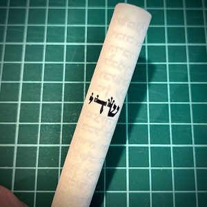Op de afbeelding: Een witte rol met Hebreeuwse tekst, waaronder het woord "Shabbat" in zwarte letters.