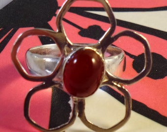 Sterling silver flower ring with an oval carnelian cabochon gemstone inset in a flower setting.