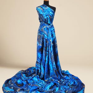 Puede incluir: Tela de impresi&oacute;n abstracta azul y dorada con un dise&ntilde;o de m&aacute;rmol. La tela est&aacute; drapeada sobre un maniqu&iacute;.