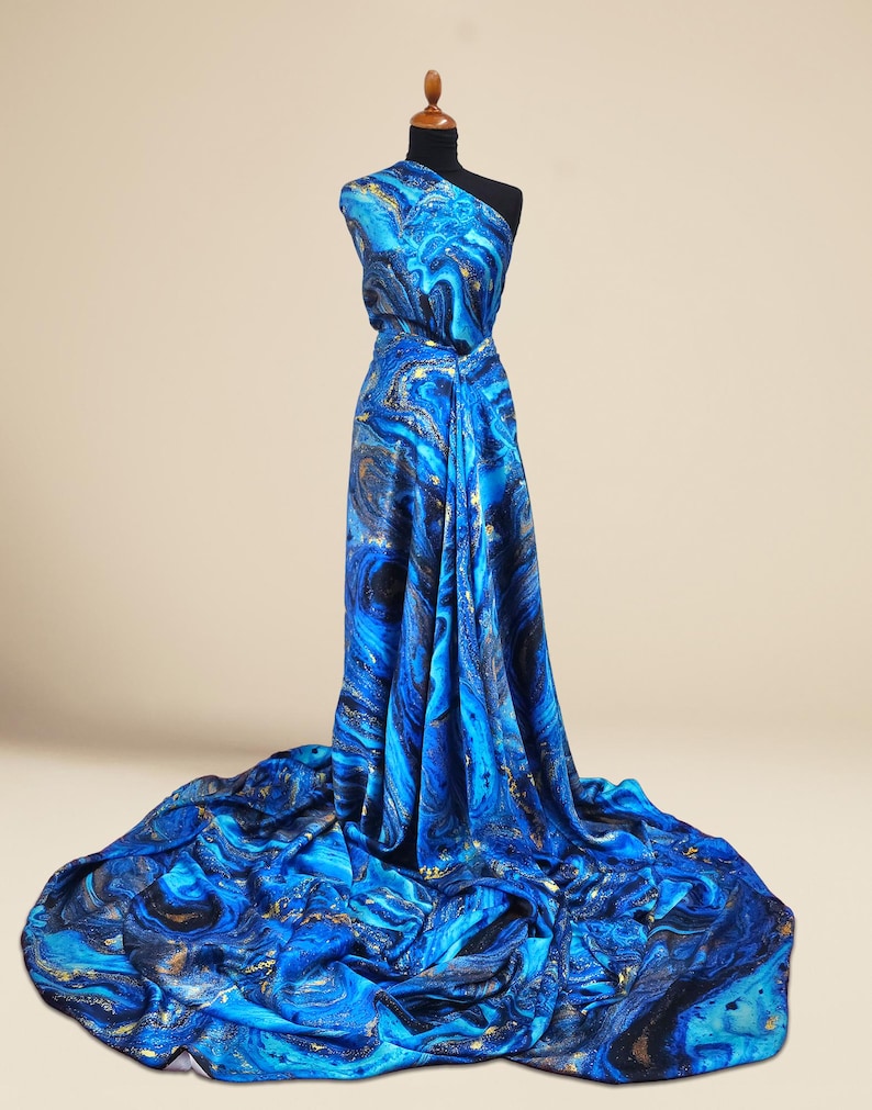 Puede incluir: Tela de impresi&oacute;n abstracta azul y dorada con un dise&ntilde;o de m&aacute;rmol. La tela est&aacute; drapeada sobre un maniqu&iacute;.