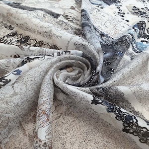 May include: A white fabric with a black and brown paisley pattern. The fabric is folded and draped, showing the intricate details of the design.