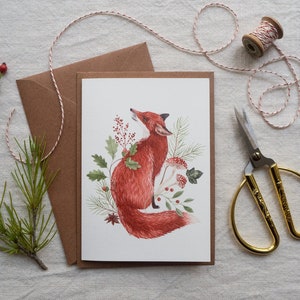 Christmas card featuring a red fox adorned with Christmas branches and red spotted mushrooms