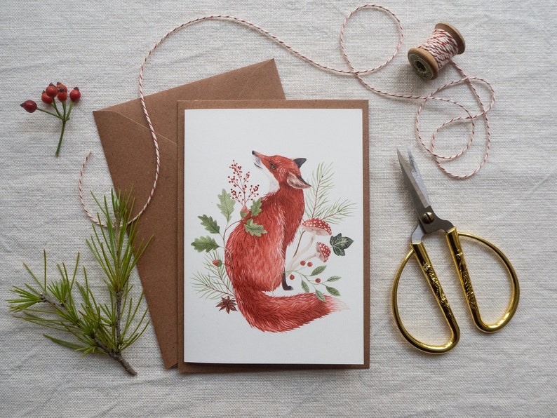 Christmas card featuring a red fox adorned with Christmas branches and red spotted mushrooms