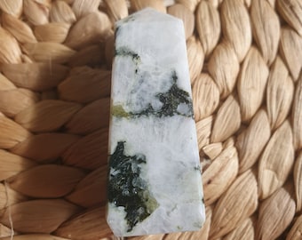 May include: A white and green crystal point with a pointed top and a flat base. The crystal has a white base with green veins running through it.