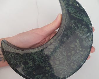 May include: A green and black crescent moon shaped stone with a swirling pattern.