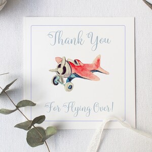 Puede incluir: Una tarjeta blanca con texto azul que dice "Gracias por volar por encima!" y una ilustraci&oacute;n de acuarela de un avi&oacute;n de juguete rojo con detalles azules.