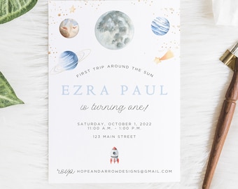 May include: A blue and white invitation card with a watercolor illustration of planets and stars. The text reads "First trip around the sun, Ezra Paul is turning one! Saturday, October 1, 2022, 11:00 AM - 1:00 PM, 123 Main Street, RSVP hopeandarrondesigns@gmail.com".