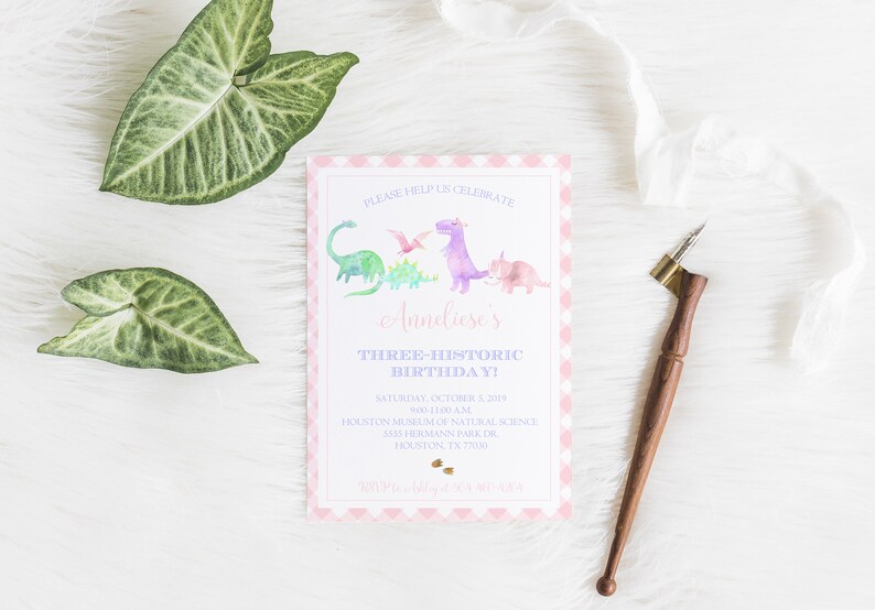 May include: Pink and white gingham invitation with a watercolor illustration of dinosaurs. The text reads "Please help us celebrate Anneliese's Three-Historic Birthday! Saturday, October 3, 2019 9:00-11:00 AM Houston Museum of Natural Science 5835 Hermann Park Dr. Houston, TX 77030"
