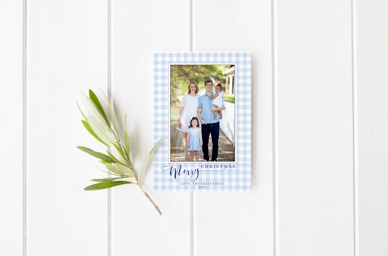 May include: A blue and white gingham Christmas card with a photo of a family of four. The text "Merry Christmas" is written in blue script. The family is standing in front of a white picket fence.