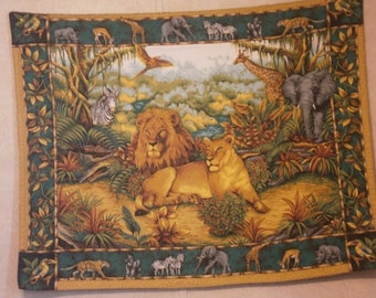 May include: A rectangular fabric panel featuring a vibrant jungle scene. A male and female lion are the focal point, surrounded by lush greenery and various African animals, including elephants, giraffes, and zebras. The border is a dark green with animal and plant motifs.