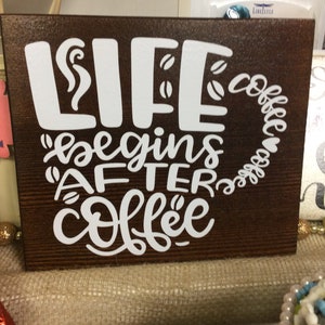 May include: A rectangular wooden sign with the phrase "LIFE begins AFTER coffee" in white lettering. The word "LIFE" is stylized with a coffee steam design, and the word "coffee" is written in a coffee cup shape.