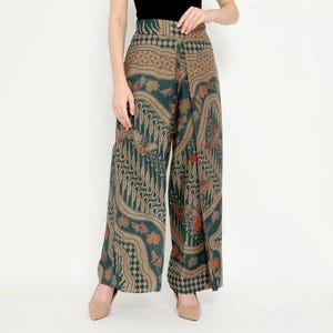 Puede incluir: Pantalón de pierna ancha con estampado batik verde y marrón. El pantalón tiene un estilo de envoltura y una cintura alta.