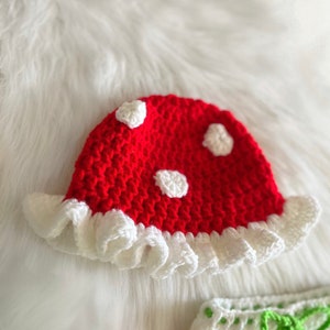 May include: A red crocheted mushroom hat with white polka dots and a white crocheted ruffle around the brim.