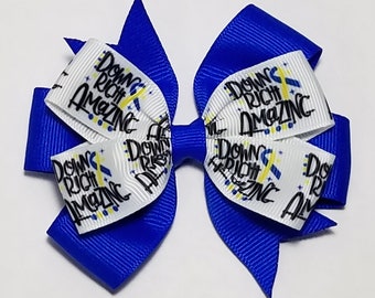 May include: A blue and white ribbon hair bow with the text "Down Right Amazing" printed on it. The ribbon is decorated with yellow and blue accents.