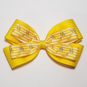 May include: A yellow hair bow with a white and yellow striped pattern and a banana print.