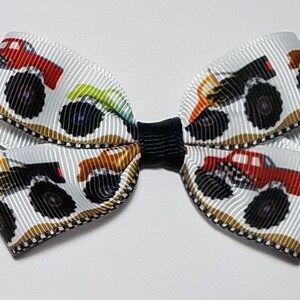May include: White hair bow with a black center and a pattern of colorful monster trucks on a white background.