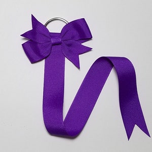 May include: Purple ribbon hair bow with a metal ring and a long tail. The bow is tied in a classic shape with two loops and a center knot.
